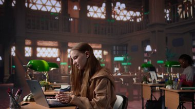 Sınav için ayrıntılı notlar okuyan ve yazan kız öğrenci, üniversitedeki bir kütüphane ortamında yapılacak konferans için siyaset bilimi okuyor. Genç yetişkin bir meslektaşına danışıyor. Kamera B.