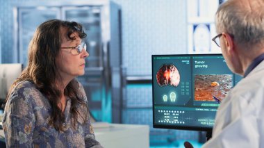 Hekim, bir hastaya MRI taraması için danışarak tümör büyümesi ve modern bir sağlık ofisindeki potansiyel kemoterapi seçenekleri hakkında bilgi veriyor. Tavsiyeler. Kamera B.