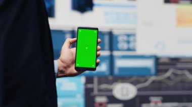 Erkek yönetici, dijital çalışma alanındaki içgörü ve analizlerle yeni büyüme stratejilerini keşfetmek için yeşil ekranlı telefonu kullanır. Modern iş zekasını ve verimliliğini temsil ediyor. Kamera A.