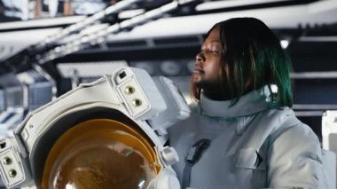 Yabancı gezegendeki yüzey görevini tamamladıktan sonra uzay istasyonunda miğfer tutan neşeli kadın astronot portresi. Gülümseyen Afrikalı Amerikalı kozmonot Dünya 'ya dönmeye hazırlanıyor, kamera B