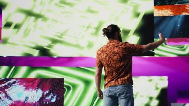 Genç kaygısız adam, modern DJ kültürünün, medya etkisinin ve dijital sanatın performansını temsil eden eğlenceli neon ışıklar ve ritimlerle çevrili selfie ve videolar çeker. Kamera B.