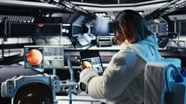Fütürist uzay gemisinin içindeki astronot rutin görev kontrolü sırasında Kızıl Gezegen yolculuk analizlerini kontrol ediyor. Uzay istasyonu kozmonotu, Mars keşif ölçümlerini gösteren monitörün yanında duruyor.