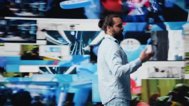 Erkek canlı sunucu izleyicilere markalaşma stratejisi ve sosyal eğilimler hakkında iletişim kuruyor, sunum sırasında mikrofon kullanarak iletişim ve küresel erişime yardımcı oluyor. Kamera B.