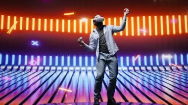 Neon ışıklı bir gece sahnesinde modern bir adam VR yüksek teknoloji gözlüğü kullanıyor, siber punk stilini somutlaştırıyor ve sanatsal vizyon yoluyla dijital ilham veriyor. Fütürist estetiğin parlak yansımaları. Kamera B.