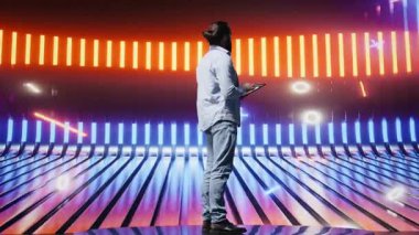 Parlayan neon ışıkların altında parlak renkler ve fütüristik bir atmosferle çevrili havalı biri duruyor. Gece hayatı sahnesinde bireysellik, kentsel tarz ve yaratıcı tavır. Kamera B.