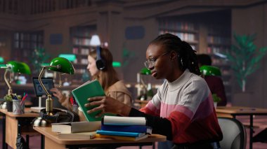 Kendine güvenen öğrenci, üniversite kütüphanesinde üniversite diploması üzerine çalışarak güvenilir kaynaklardan bilgi ve celp topluyor. Akıllı kız ders çalışıyor. Kamera A.