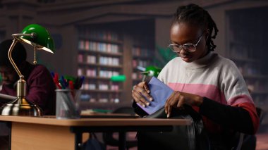 Afrikalı Amerikalı bir öğrenci kütüphane koleksiyonu veritabanındaki notlarla karşılaştırıyor ve bir edebiyat ödevine odaklanmak için dizüstü bilgisayar kullanıyor. Diploması için çalışan genç bir öğrenci. Kamera A.