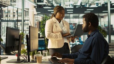 Ofisteki işçiler dizüstü bilgisayarda yapılan işlere bakan yöneticilerden geri bildirim alıyorlar. İş yerinde Afrikalı Amerikalı yönetici çalışanlara görev veriyor, gerekli verileri sağlıyor, kamera B