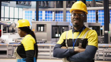 Güneş paneli üretim hattı ekipmanlarını denetleyen teknisyen portresi. Otomatik sanayi 4.0 fabrikasında bilgisayar ve kamera A kullanarak fotovoltaik montaj sistemleri sürdüren Afrikalı Amerikalı bir adam.