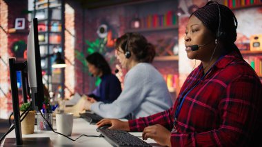 Müşterilere adım adım rehberlik eden mutlu çağrı merkezi ajanı. PC masasında gülümseyen müşteri merkezi çalışanı arama sırasında müşterileri teknik çözümler üzerinden yürütüyor, kamera B