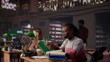 Kendine güvenen öğrenci, üniversite kütüphanesinde üniversite diploması üzerine çalışarak güvenilir kaynaklardan bilgi ve celp topluyor. Akıllı kız ders çalışıyor. Kamera B.