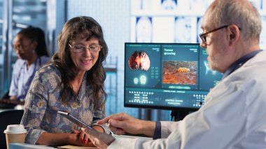 Pratisyen hekim yaşlı kadın hastaya teşhis testi sonuçları hakkında danışır, bir klinikte doğru rapor ve bakım yönetimi için tıbbi teknolojiden yararlanır. Sağlık hizmeti sağlayıcısı. Kamera B.