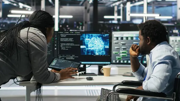 Tekerlekli sandalyedeki yönetici ve veri merkezindeki iş arkadaşı, kapatma süresini en aza indirmek için yapay zeka ağacı yazılımı kullanıyor. Sunucu merkezi engelli bilişim uzmanı ve iş arkadaşı görsel programlama uygulaması kullanarak, kamera B