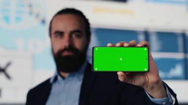 Erkek uzman, şirketin performansını ve gelecekteki başarısını optimize eden gösterge paneli, finansal eğilimler ve KPI ölçümleri yanında izole edilmiş görüntülü telefon kullanır. Liderlik. Kamera A.