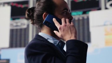 Akıllı telefon görüşmesinde uzman işadamı finans ve analizi tartışıyor, şirket stratejisi kuruyor. Veri tablolarıyla çevrili, dijital yenilik ve şirket büyümesi planlanıyor. Kamera A.