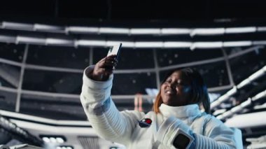Neşeli astronot akıllı telefon kamerasıyla yıldız gemisinde selfie çekerken eğleniyor. Uzay istasyonunda kozmonot kozmik yolculuk sırasında cep telefonuyla fotoğraf çekiyor, kamera B