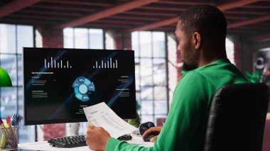 Siyah serbest çalışan, iş konferansını PC monitöründen izliyor, istatistik tablolarına bakıyor. Apartman ofisindeki uzaktan çalışan bilgisayardaki sunum grafiklerini takip ediyor. Kamera A.