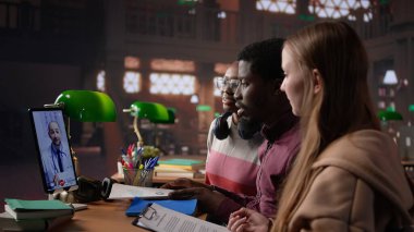 Çeşitli öğrenci grupları doktorlarla bir video görüşmesi yapıyor, tıbbi konuları ve yöntemleri öğreniyorlar. Tıp öğrencileri kütüphanede uzaktan eğitim için teletıp aletleri kullanıyorlar. Kamera B.