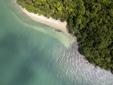 Sahilde yelkenli teknesi olan tropikal kumlu bir sahil manzarası, altın kumu olan güzel bir plaj manzarası. Kıyıdaki mavi sularda yumuşak kum ve çarpıcı bir deniz manzarası olan bir tekne yanaştı..