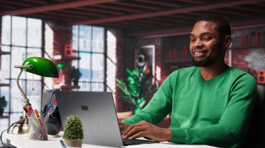 Evdeki siyah tele-sekreter belgeleri düzenlemek ve günlük görevleri çözmek için dizüstü bilgisayar açıyor, raporları ve dosyaları güncelliyor. Uzaktan kumandalı ve dijital evrak işleriyle uğraşan genç bir çalışan. Kamera A.