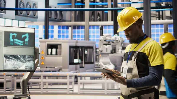 Akıllı fabrika teknisyeni donanımı değiştirmeden önce IoT sensörleri verilerini analiz etmek için tablet kullanıyor. Endüstri 4.0 'daki Afrikalı Amerikalı adam devre dışı kalma süresini azaltmak için sistem kontrolü yapıyor. Kamera A.