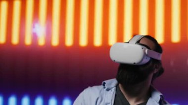 Tarz sahibi genç adam, sanal gerçeklik kulaklığı kullanarak sanatsal titreşimleri yansıtıyor. Çevresi, eğlenceden esinlenilmiş siber bir atmosferde renkli neon ışıklarla çevrili. Gece hayatı minimalizmi. Kamera A.