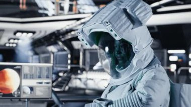 Uzay giysisi içindeki kadın astronot uzayda insan genleşmesi yapan uzay aracının içindeki bilek cihazını kontrol ediyor. Yıldız gemisi mürettebatı, insanlığın uzun süreli hayatta kalmasını destekleyen operasyonlara hazırlanıyor, kamera B