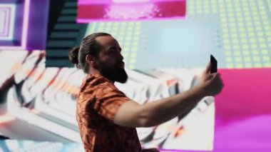 Akıllı telefonunu neon ışıkların altında kullanan rahat adam içerik yaratıcısı ve DJ olarak fotoğraf ve videoları yakalıyor. Modern tasasız insan gece hayatı sahnesinde görsel sanattan hoşlanır. Kamera A.