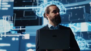 Erkek iş adamı yapay zeka stratejisi ve otomasyon araçları üzerine çalışıyor. Veri görselleştirmesi, sinirsel ağlar ve bulut hesaplamalarıyla çevrili olarak, akıllı teknolojiyi keşfeder. Kamera A.