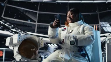 Mutlu dişi kozmonot galaksi gezisi sırasında akıllı telefon kullanarak ailesiyle görüntülü görüşme yapıyor. Afrikalı Amerikalı kadın, uzay gemisinde cep telefonu kullanarak sevdikleriyle uzaktan görüşme yapıyor.