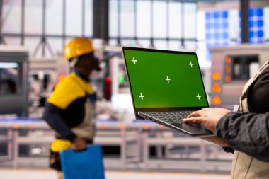Endüstri 4.0 uzmanı akıllı imalat tesisinde izole edilmiş kromakey şablona sahip dizüstü bilgisayar tutuyor. Otomatik fabrika dijital arayüzler, robotik kollar ve ileri üretim hattı kullanır..