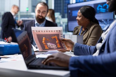 Endüstriyel fabrika yöneticileri şemaları inceler, dizüstü bilgisayarları kullanarak tesisleri güncellerler. Fabrika hissedarları taşıyıcı bant planlarına bakıyor, defter aygıtı üzerinde çalışıyorlar