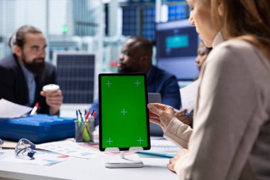 Fabrika çalışanı güneş paneli otomasyon stratejilerini tartışan yöneticilerin yanında izole ekran tabletinde çalışıyor. İşçi takım geliştirme süreçlerinin yanında krom anahtar aygıtı kullanır, kapat