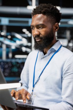 Sunucu odasındaki bilgisayar bilimcisi veri yedekleme çözümlerini uygulamak ve yönetmek için dizüstü bilgisayar kullanır. Veri merkezindeki Afrikalı Amerikalı adam teknik hataları tanımlıyor ve çözüyordu.