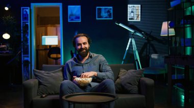 TV 'de film izlerken ve patlamış mısır yerken evde yemek yiyen bir adam. Yemek yerken boğazı tıkanan, koltukta heimlich manevrası yapan, hayatı için savaşan, kamera B