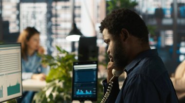 Ofisteki işçileri müşterilerle konuşmak için sabit telefonu kullanarak kapatın. İş yerinde çalışan Afrikalı Amerikalı bir çalışan çağrı sırasında iş ortağıyla tartışıyor, performans ölçümlerini analiz ediyor, kamera A