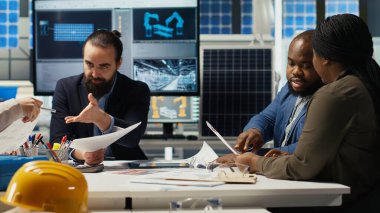 Mühendisler güneş paneli montaj hatlarının ayrıntılı şemalarını inceliyor, üretim planlarını ve verimlilik için bileşen yapılandırmalarını inceliyor, yeni prototipler için özet dökümanlar hazırlıyor, kamera B