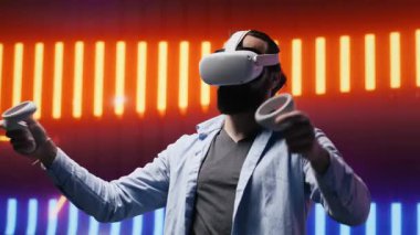 Havalı bir genç, neon ışıkların altında VR teknolojisiyle eğleniyor, siber punk stilini somutlaştırıyor ve sanatsal vizyon için renkli bir ilham kaynağı oluyor. Estetiğin parıldayan yansımaları. Kamera A.