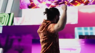 Parlayan neon ışıklarının altında dans eden havalı dijital içerik yaratıcısı, ritim ve bireyselliği ifade ediyor. Modaya uygun müzik ve sanatsal görsellerle çevrili, enerji ve retro stil getiriyor. Kamera A.