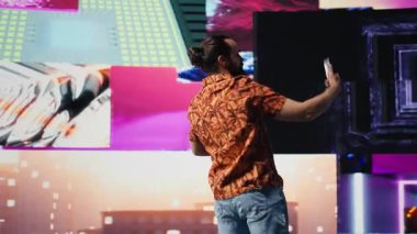 Akıllı telefonunu neon ışıkların altında kullanan rahat adam içerik yaratıcısı ve DJ olarak fotoğraf ve videoları yakalıyor. Modern tasasız insan gece hayatı sahnesinde görsel sanattan hoşlanır. Kamera B.
