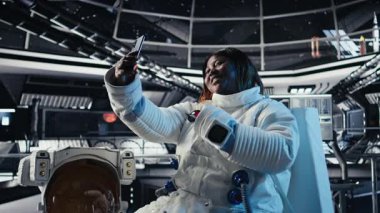 Neşeli astronot akıllı telefon kamerasıyla yıldız gemisinde selfie çekerken eğleniyor. Uzay istasyonunda kozmonot kozmik yolculuk sırasında cep telefonuyla fotoğraf çekiyor.