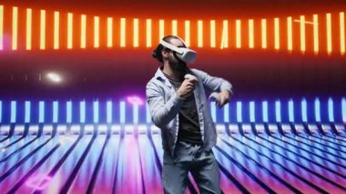 Tarz sahibi genç adam, sanal gerçeklik kulaklığı kullanarak sanatsal titreşimleri yansıtıyor. Çevresi, eğlenceden esinlenilmiş siber bir atmosferde renkli neon ışıklarla çevrili. Gece hayatı minimalizmi. Kamera B.