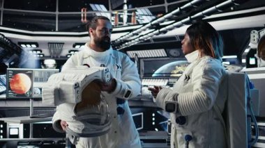 Astronot, uzay istasyonu dışındaki planlanmış operasyonlara çıkmadan önce kaskını takıyor ve meslektaşıyla yumruk tokuşturuyor. Kozmonot gezegene indikten sonra uzay gemisinden ayrılmaya hazırlanıyor. Kamera A.