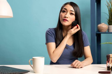 Profesyonel makyöz masasında oturuyor ve yayın sırasında farklı fırça teknikleri gösteriyor. Asyalı güzellik içeriği yaratıcısı kozmetik aletlere odaklanan bir yaşam formu kaydetti.