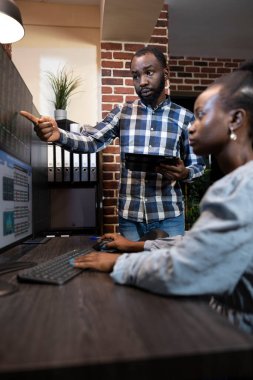 Masada çalışan kadın ve erkek ön x danışmanları gece geç saatlerde birden fazla ekranda borsa verilerini analiz ediyorlar. Ofiste bir tuğla duvar ve profesyonel çalışma istasyonu bulunuyor..