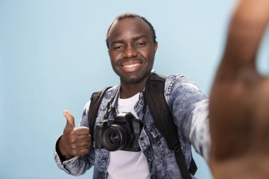 Afrikalı Amerikalı erkek vlogger çevrimiçi seyircisine başparmak işareti yapıyor, kendini stüdyoda kaydediyor. Bir grup neşeli siyah fotoğrafçı kameraya doğru bir anlaşma jesti yapıyor..