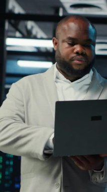 Bakım sırasında yapay zeka otomasyonunu kullanarak veri merkezinde yürüyen dikey video mühendisi. Afro-amerikan sunucu merkezi çalışanı donanım donanımlarında derin öğrenme modelleri yapılandırıyor, kamera B