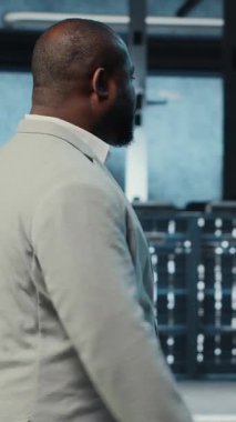 Dikey video çalışanı yüksek teknoloji veri merkezinde web sitelerine ev sahipliği yapmak için kullanılan donanımla yürüyor. Bilgi İşlem uzmanı loş ışıklandırmalı sunucu çiftliği kurulumunu denetlemesi şirketlerin bağlı kalmasına yardımcı oluyor, kamera B