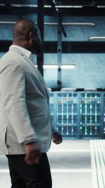 Dikey video çalışanı yüksek teknoloji veri merkezinde web sitelerine ev sahipliği yapmak için kullanılan donanımla yürüyor. Bilgi İşlem uzmanı loş ışıklandırmalı sunucu çiftliği kurulumunu denetlemesi şirketlerin bağlı kalmasına yardımcı oluyor, kamera A