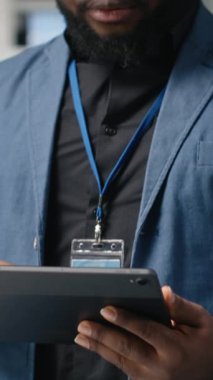 Bir güneş enerjisi üretim tesisinde çalışan dikey video Afrikalı Amerikalı teknisyen şirket denetimi ve ekipman üretimini yansıtmak için takım elbise giymiş operasyonları değerlendiriyor. Temiz enerji. Kamera.